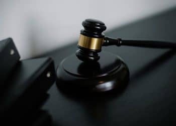 Um martelo de juiz de madeira com detalhes dourados, repousando sobre uma base redonda escura em uma mesa, simbolizando justiça, lei e autoridade.
