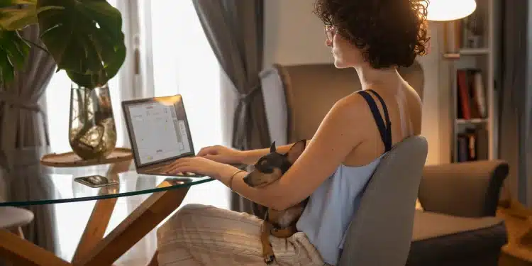 Pessoa trabalhando em casa no computador com cachorro de estimação no colo, ilustrando profissões home office.