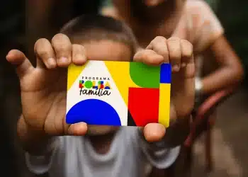 Mãos de uma criança segurando o cartão do Programa Bolsa Família em foco, simbolizando o impacto direto dos pagamentos nas famílias beneficiárias a partir de 20 de outubro.