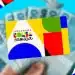 Mão segurando cartão colorido do Programa Bolsa Família com várias notas de dinheiro azul em fundo desfocado