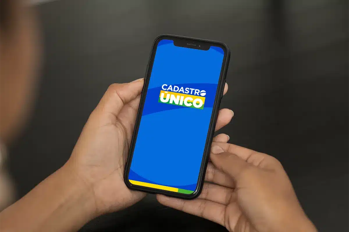 Aplicativo do Cadastro Único no Celular Mãos segurando smartphone com tela azul exibindo logo do Cadastro Único.