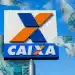 Placa da Caixa Econômica com cédulas de 100 reais ao redor em fundo de céu azul