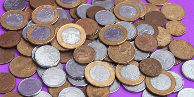 Imagem de moedas do Real espalhadas, com destaque para a moeda de 1 Real de 2018, que pode ser rara devido a erro de cunhagem.