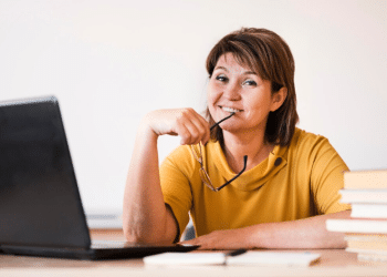 Mulher madura sorrindo e estudando em frente a um laptop, simbolizando a requalificação profissional e a busca pelo primeiro emprego após os 40 anos através de cursos gratuitos.
