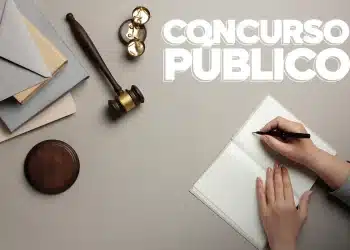 Mulher se preparando para um concurso público, com caneta na mão e um caderno, ao lado de um martelo e uma balança da justiça.