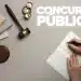 Mulher se preparando para um concurso público, com caneta na mão e um caderno, ao lado de um martelo e uma balança da justiça.
