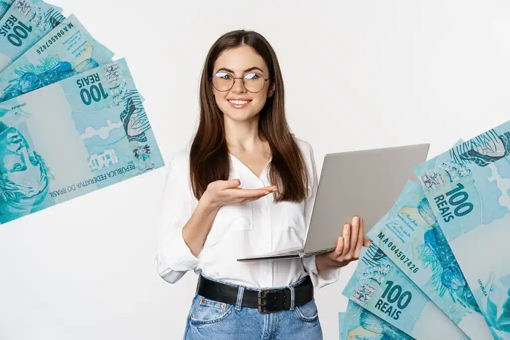Carreiras de sucesso sem diploma Imagem ilustrativa de uma mulher segurando um notebook e sorrindo enquanto exibe cédulas de R$100, ilustrando o sucesso financeiro sem a necessidade de diploma universitário.