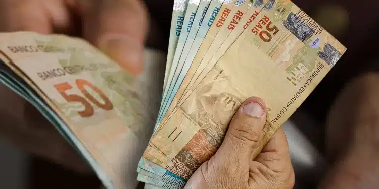 Mãos segurando e contando várias notas de dinheiro em reais com destaque para notas de 50 e 20