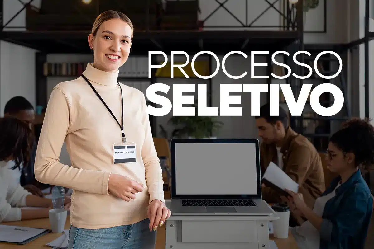 Processo Seletivo INSS: Requisitos e Prazo Final (21/10) para Inscrição de Estudantes no CIEE Jovem sorridente com crachá em frente a um notebook, representando a estudante que atende aos requisitos do Processo Seletivo do INSS, como matrícula em ensino médio ou superior.
