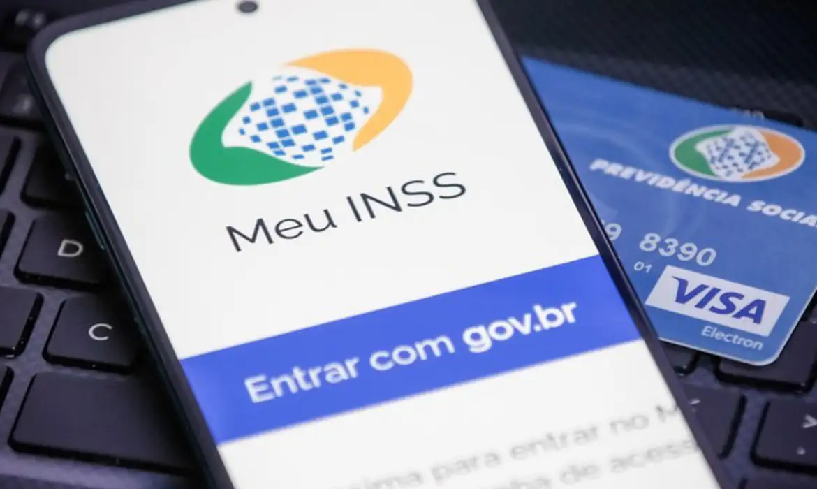 Aplicativo Meu INSS Tela de celular com app Meu INSS e cartão da Previdência Social Visa sobre teclado