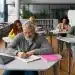 Grupo de adultos sentados em mesas em uma sala de aula moderna, focados em estudar e escrever em cadernos