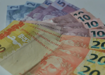 Cédulas de dinheiro em reais brasileiros com notas de 5, 10 e 20 reais espalhadas sobre superfície clara.