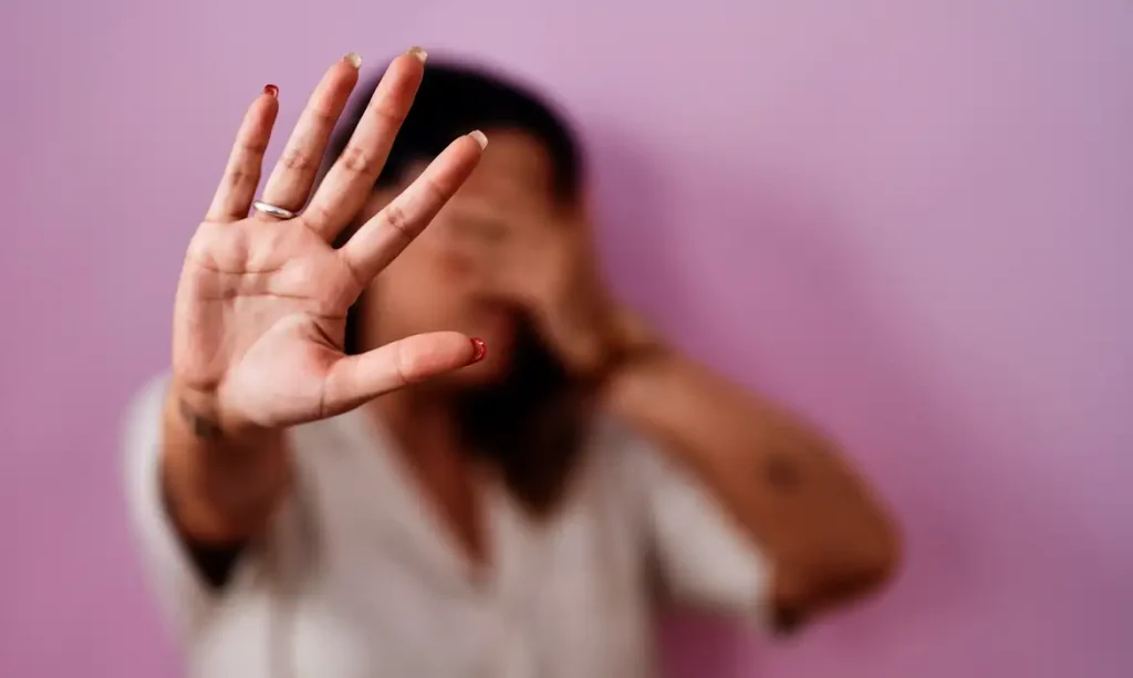 Vagas de emprego para mulehres vítimas de violência. Mulher em situação de violência doméstica, com gesto de proteção, simbolizando a luta contra a violência.