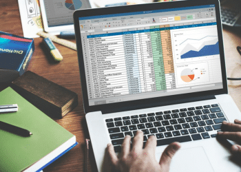 Pessoa trabalhando em um notebook que exibe uma complexa planilha de dados e gráficos no Microsoft Excel, simbolizando a análise corporativa e o uso da ferramenta no dia a dia profissional.