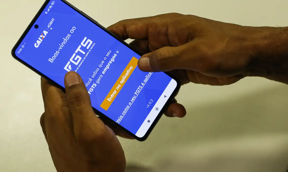 FGTS saque calamidade Pessoa segurando smartphone com o aplicativo FGTS da Caixa aberto na tela