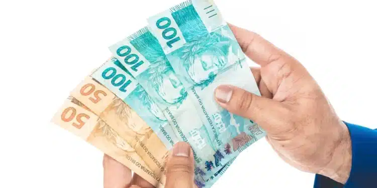 Mãos segurando cédulas de real representam o Saque Calamidade do FGTS, que permite a retirada de até R$ 6.220.