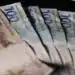 Imagem ilustrativa de cédulas de R$ 100 e R$ 200 abertas em leque sobre fundo escuro, em referência ao pagamento do INSS no fim de 2026