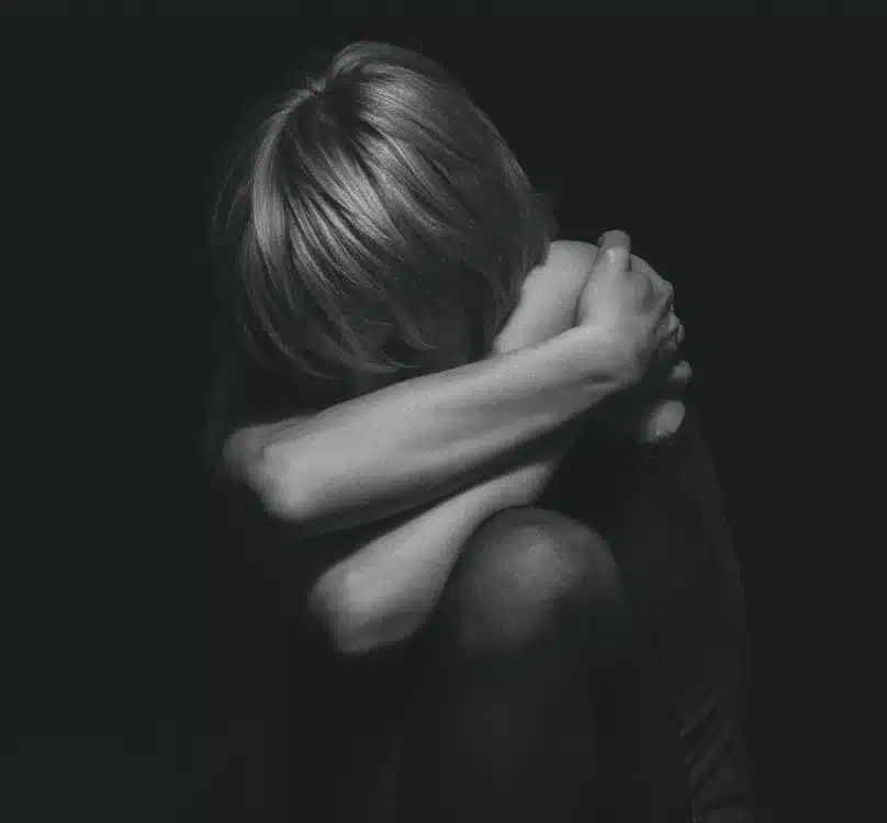 Reflexão sobre o impacto emocional da infância Pessoa em um momento de introspecção, com os braços abraçando as pernas, mostrando vulnerabilidade e sentimentos profundos.