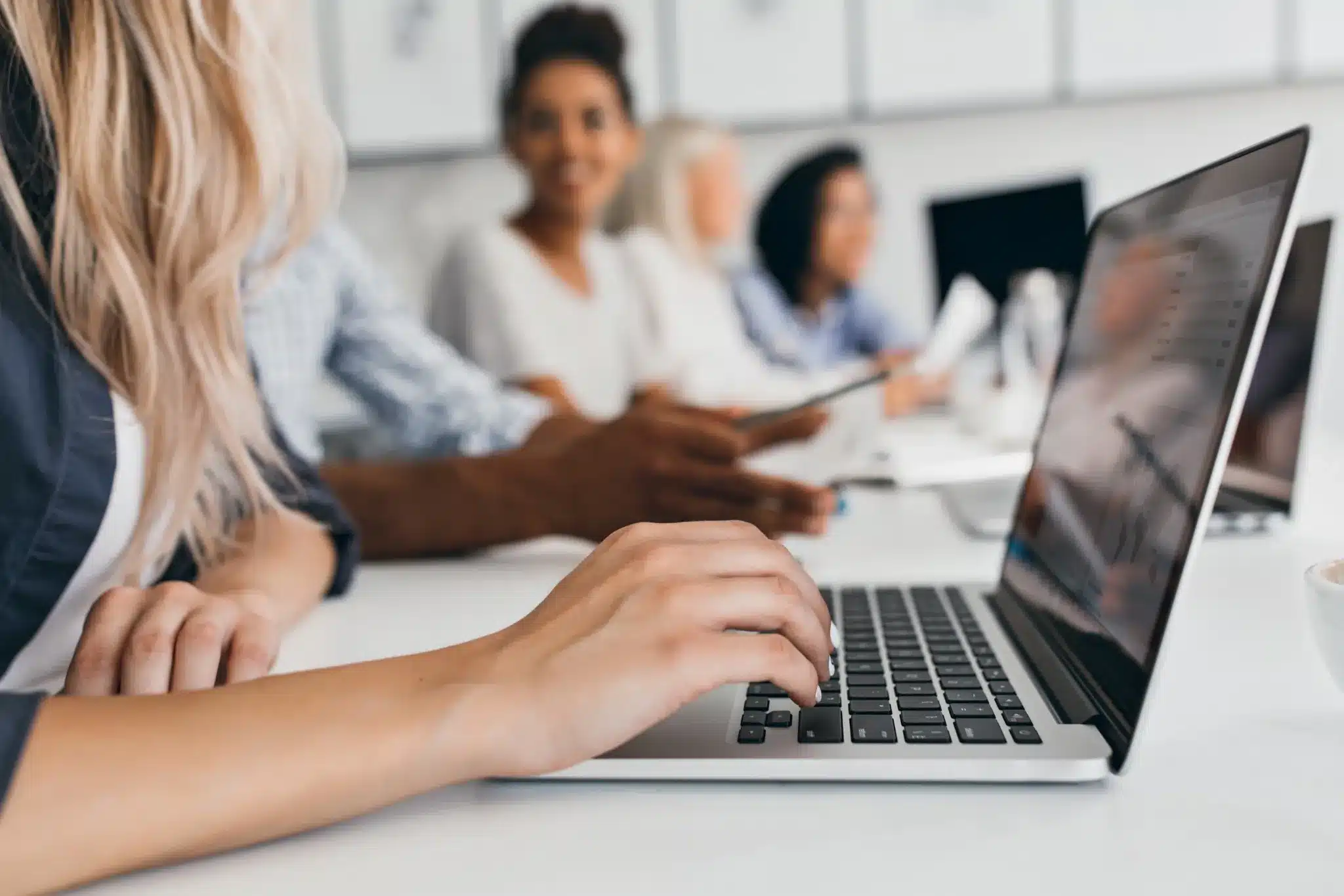 Pessoas trabalhando em equipe com laptop moderno Mãos de pessoa digitando em laptop durante reunião de equipe com colegas ao fundo em escritório moderno