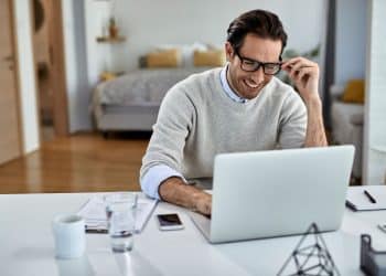 Homem-feliz-trabalhando-de-casa-em-home-office-com-notebook-para-artigo-sobre-profissões-que-pagam-em-dólar-2025
