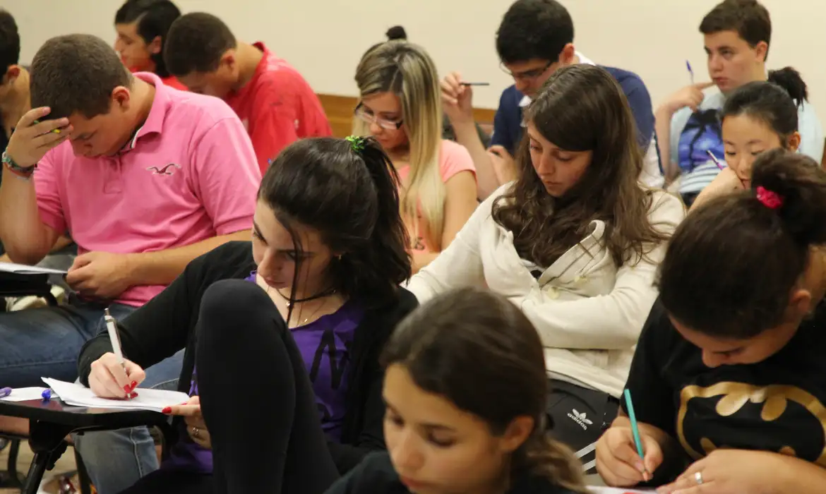 Prova CNU 2025 Alunos em sala de aula concentrados escrevendo em cadernos durante uma prova