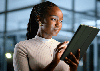 Profissional de sucesso, mulher em escritório noturno, usando tablet para analisar dados e otimizar estratégias de alta performance.