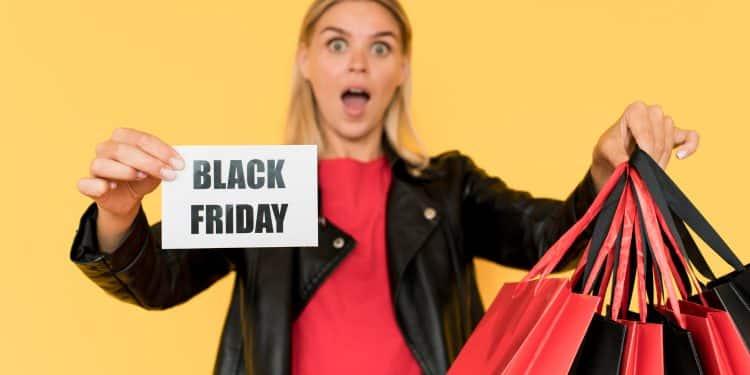 Mulher loira segurando cartão escrito Black Friday e várias sacolas vermelhas e pretas.