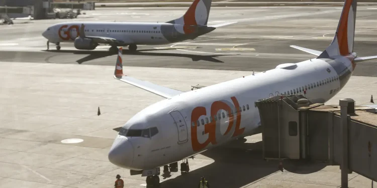 Dois aviões da Gol estacionados no aeroporto com um ligado à ponte de embarque