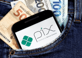 Cédulas de real e celular com logo do Pix dentro do bolso de uma calça jeans