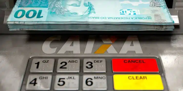 Dinheiro (notas de R$ 100) sendo sacado em caixa eletrônico da CAIXA. Ilustra o Saque do FGTS Calamidade para moradores de cidades afetadas por desastres naturais.