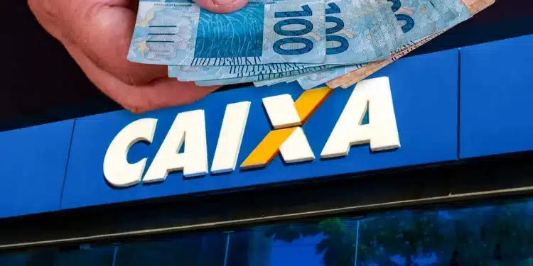 Mão segurando notas de dinheiro reais com fachada da Caixa Econômica Federal desfocada ao fundo