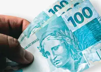 Trabalhador segurando cédulas de cem reais representando primeira parcela do 13º salário 2025