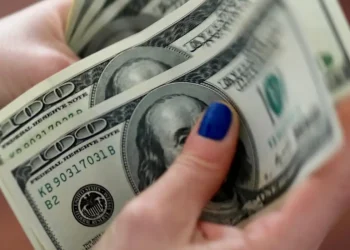 Mãos femininas com unhas azuis segurando várias notas de cem dólares americanos