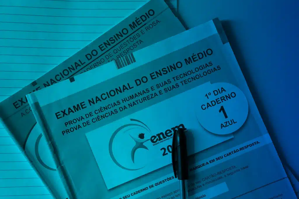 Caderno de Questões do Enem e Dicas de Documentação Cadernos de Questões Azuis e Rosa do Exame Nacional do Ensino Médio (ENEM) sobre uma folha, com uma caneta preta por cima.