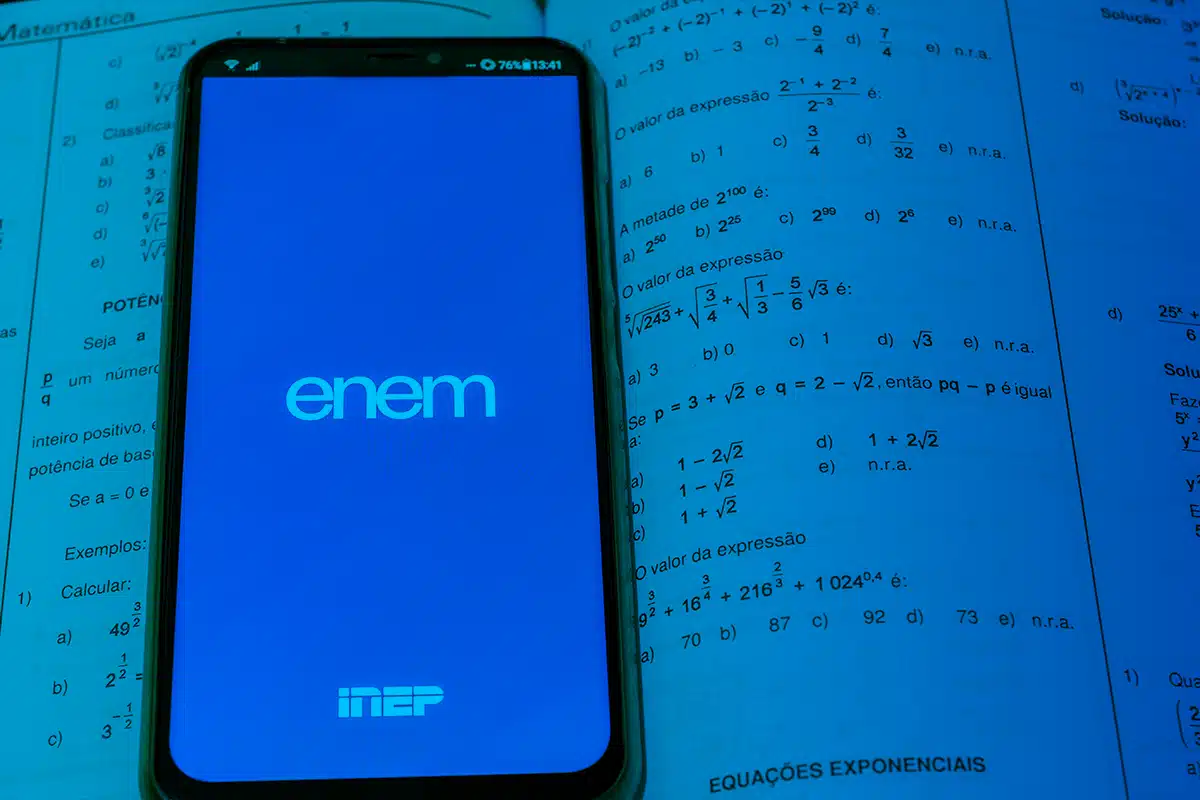 Enem Celular mostrando tela do aplicativo ENEM aberto sobre apostila de matemática com exercícios e fórmulas.