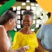 Três idosos sorrindo e interagindo alegremente em ambiente externo com fundo colorido