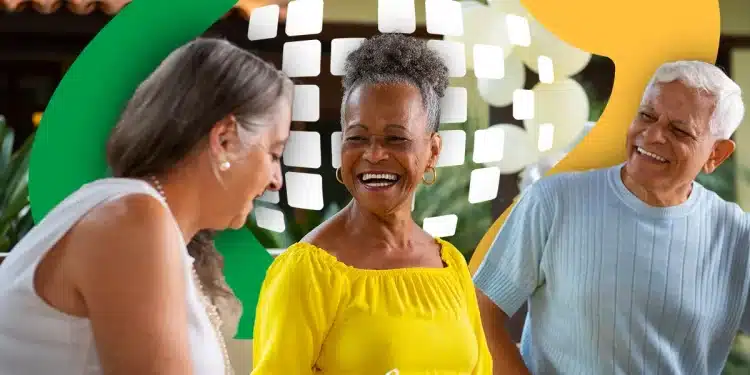 Três idosos sorrindo e conversando em ambiente externo com decoração colorida ao fundo