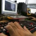 Mão digitando em teclado iluminado vermelho com laptop e equipamentos eletrônicos ao fundo