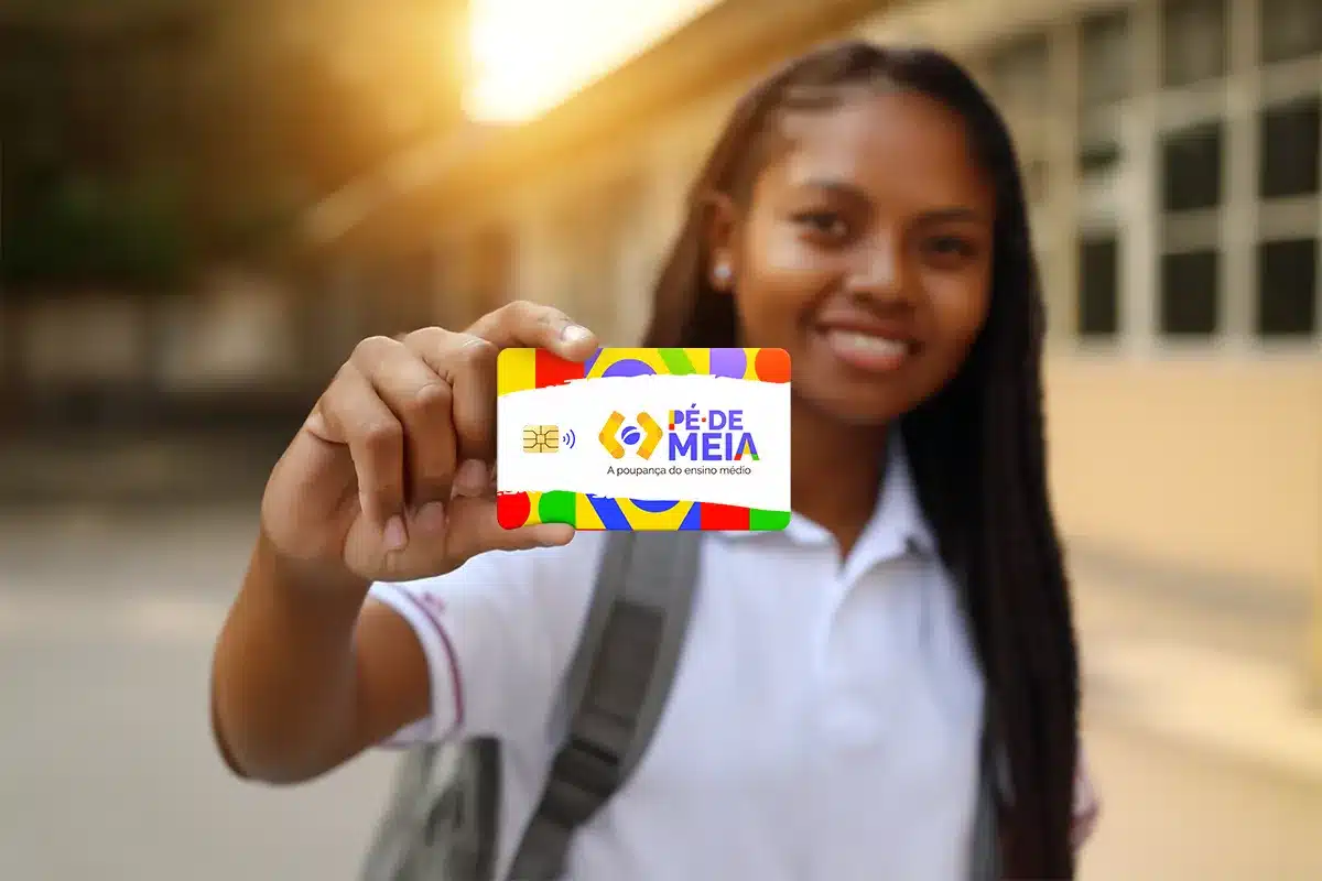 Cartão Pé de Meia para Estudantes do Ensino Médio Jovem estudante segurando cartão colorido Pé de Meia com logo e chip em fundo desfocado