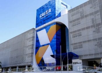 Fachada de prédio da Caixa Econômica Federal com logo grande e moderna em vidro azul.