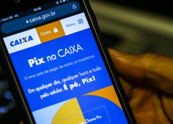 Tela de celular mostrando o site da Caixa com informações do Pix, segurado por uma mão.