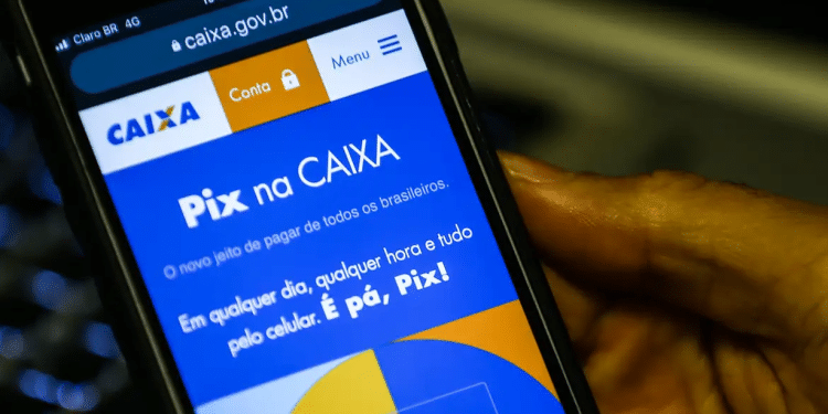 Tela de celular mostrando o site da Caixa com informações do Pix, segurado por uma mão.