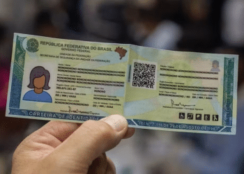 Pessoa segurando carteira de identidade brasileira com informações e QR code visíveis.