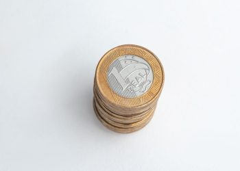 Pilha de moedas brasileiras de 1 Real sobre uma superfície branca, representando um valor potencial oculto no troco do dia a dia.