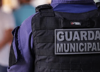 Guarda Municipal vista de costas usando colete tático preto e uniforme azul.