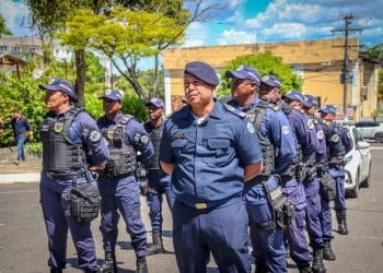 Grupo de guardas municipais uniformizados em formação ao ar livre em dia ensolarado com árvores e prédios ao fundo