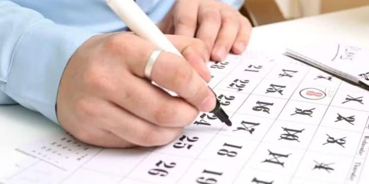 Detalhe de uma pessoa usando uma caneta para marcar datas em um calendário de papel, ilustrando a organização de folgas para o feriado de 20 de novembro (Consciência Negra) em 2025.