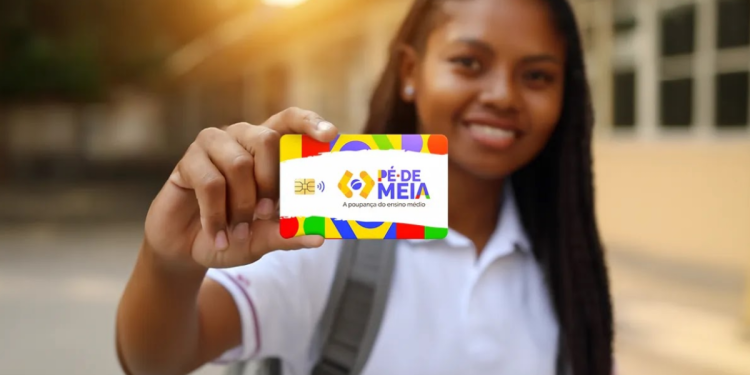 Estudante segurando um cartão do programa Pé-de-Meia com fundo escolar desfocado.