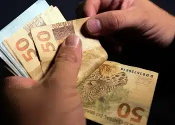 Trabalhador contando dinheiro da segunda parcela do 13º salário com descontos aplicados.