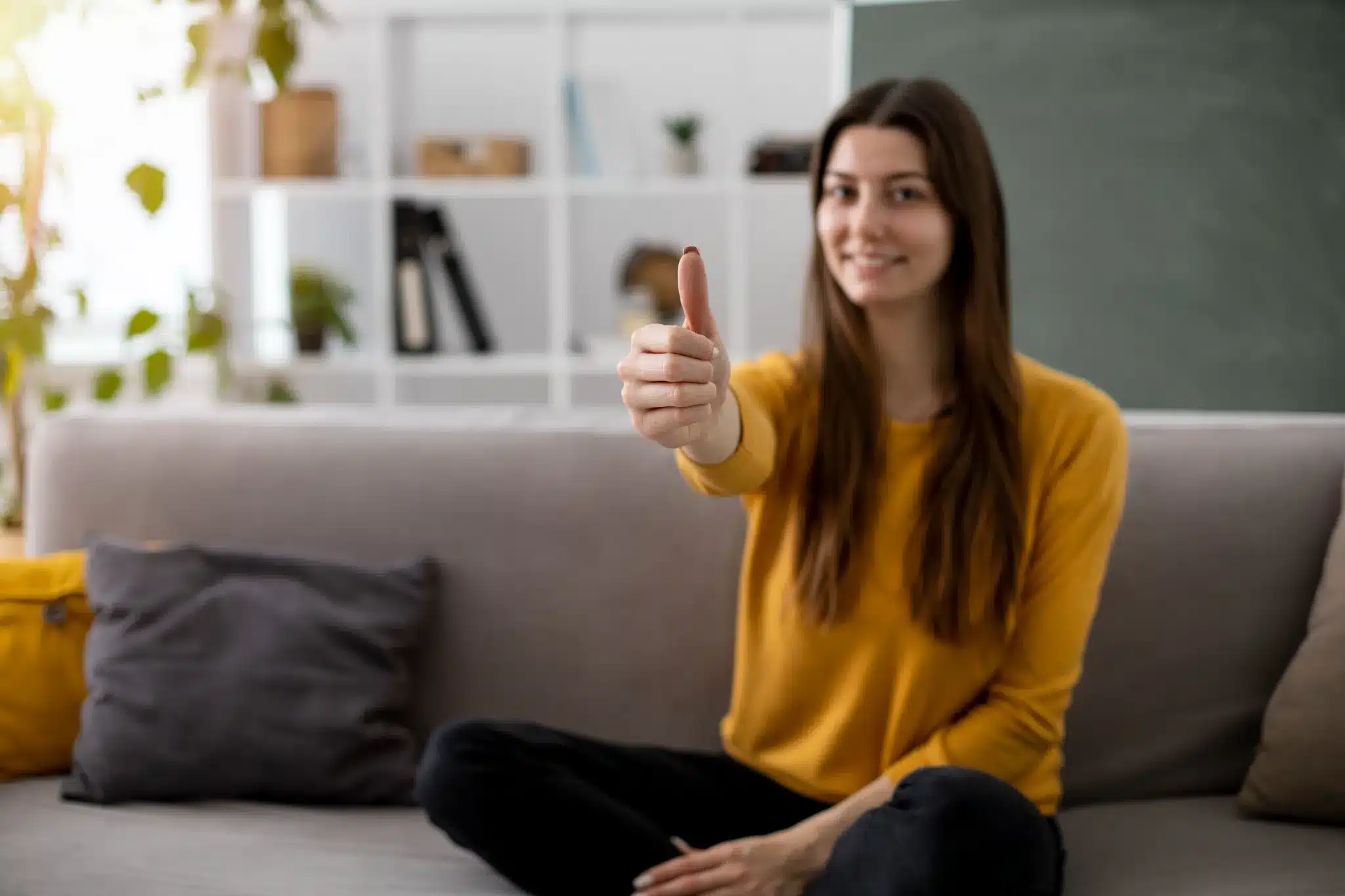 Sinal de Aprovação no Sofá Pessoa sentada no sofá fazendo sinal de positivo com o polegar.